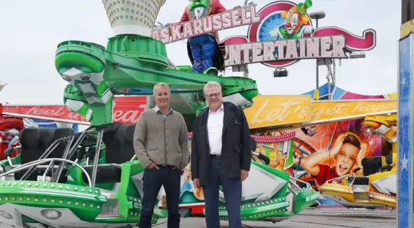Zwei Männer stehen vor einer bunten Kirmesattraktion mit Clowns und der Aufschrift "Entertainer". Ein fröhlicher Ausblick auf das Bayreuth Herbstfest.