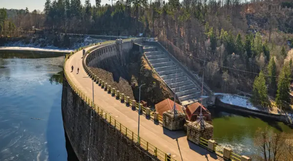 Spacerowicze na trasie zapory Pilchowice. Majestatyczna konstrukcja z kamienia i betonu otoczona lasem.