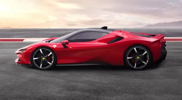 Czerwone Ferrari SF90 na torze wyścigowym, z czarnym dachem i felgami. Słońce zachodzi za górami.