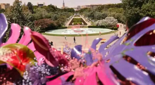 Flores vibrantes en primer plano, con el parque grande Zaragoza florece al fondo, destacando una fuente y senderos verdes.