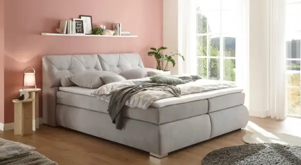 Einladendes, graues Boxspringbett mit gestepptem Kopfteil, das Ruhe und Harmonie ausstrahlt – perfekt für ein Feng Shui Bett.