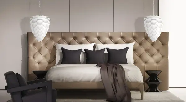 Elegancka lampa sufitowa do sypialni w kształcie szyszki, wisząca nad luksusowym łóżkiem z pikowanym zagłówkiem.