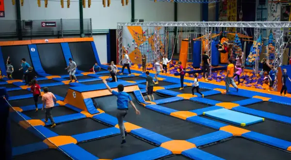 Dzieci skaczą na trampolinach w największym parku trampolin w Polsce. W tle widać ściankę wspinaczkową i tor przeszkód.