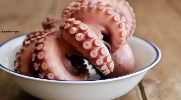 Un poulpe cuit, prêt pour une délicieuse recette. Ses tentacules aux ventouses sont mis en valeur dans un bol blanc sur fond de bois.