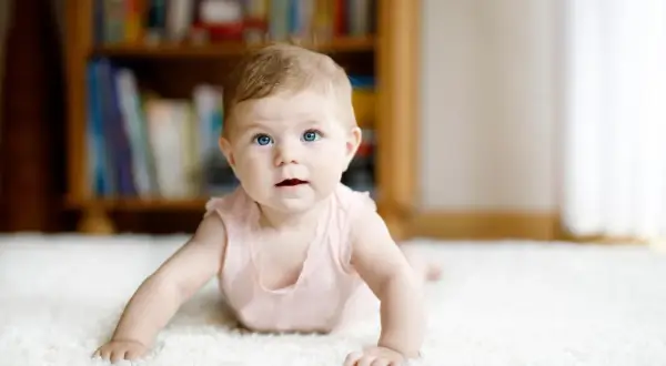 Niebieskooka dziewczynka na dywanie, odkrywająca świat zgodnie z kalendarzem skoków rozwojowych.
