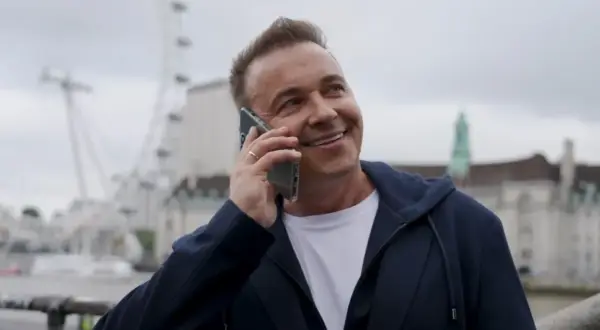 Uśmiechnięty mężczyzna rozmawia przez telefon. W tle widać London Eye. Weekend, halo, tu Londyn!