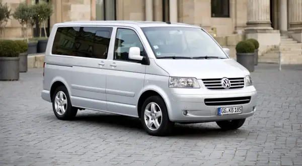 Srebrny Volkswagen T5 na brukowanym placu przed budynkiem z kolumnami.