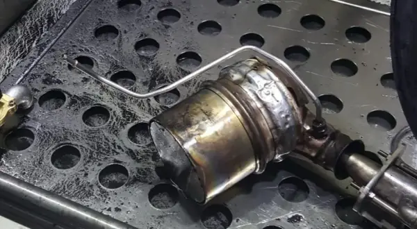 Metalowy element układu wydechowego z widocznymi śladami zużycia i zabrudzeń.