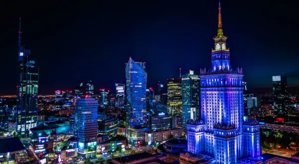 Nocna panorama Warszawy z Pałacem Kultury oświetlonym na niebiesko. Miasto tętni życiem, a liczne światła zapowiadają ciekawe warszawa wydarzenia.