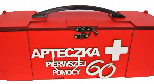 Czerwona, drewniana apteczka z napisem "Apteczka pierwszej pomocy" i białym krzyżem. Idealny prezent dla 60-latki.