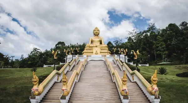Goldene Buddha-Statue über einer langen Treppe mit Naga-Schlangen-Geländern in Nakhon Si Thammarat.