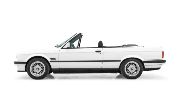 Vit cabriolet, en klassisk bmw 80 tal, med taket nere. Perfekt för sommarvägar.