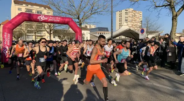 Départ d'une course à Bourg-en-Bresse sous un ciel bleu. Des coureurs s'élancent sous une arche rose.