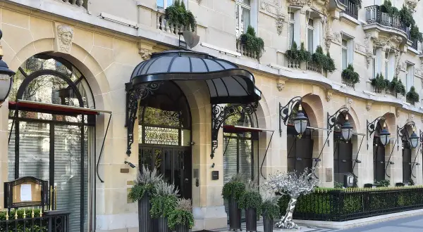 L'elegante ingresso di un edificio parigino, forse sede di Alain Ducasse a Parigi, con lampioni classici e piante verdi.