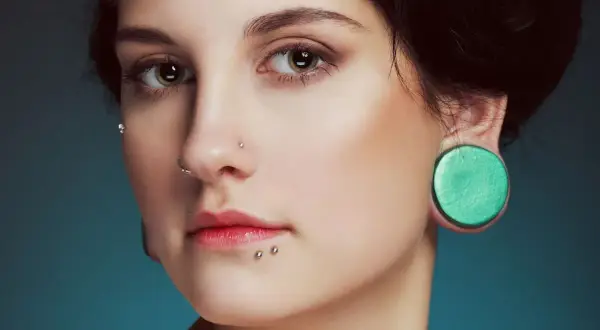 Kobieta z piercingiem w nosie, ustach i uchu. Jej ozdoby przypominają ślady po ukąszeniach pająka.