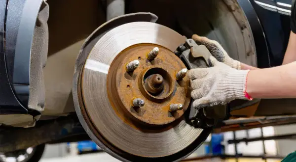 Gros plan sur un disque de frein rouillé et une plaquette de frein usée, tenue par une main gantée, prête pour le remplacement.