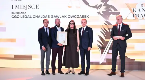 Cztery osoby w garniturach i sukience stoją na scenie, odbierając nagrodę.