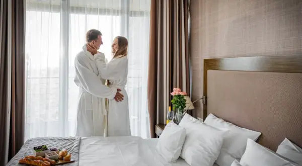 Para w szlafrokach przy oknie, romantyczny pokój hotelowy z łóżkiem i śniadaniem.