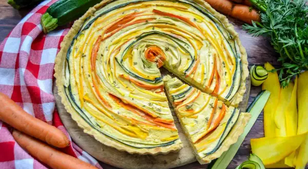 Bunte quiche vegetarisch mit Zucchini und Karotten, kunstvoll im Kreis arrangiert. Daneben frisches Gemüse.