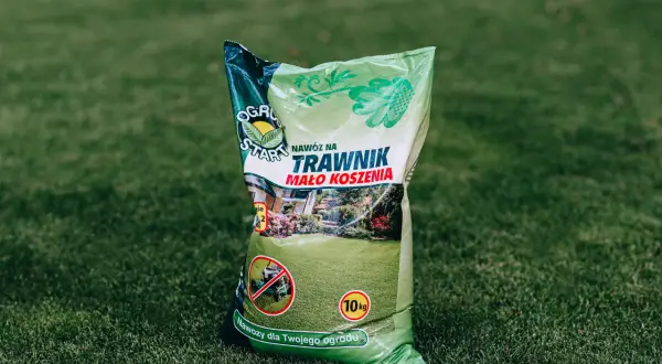 Zielona torba z nawozem do trawnika na tle trawy.