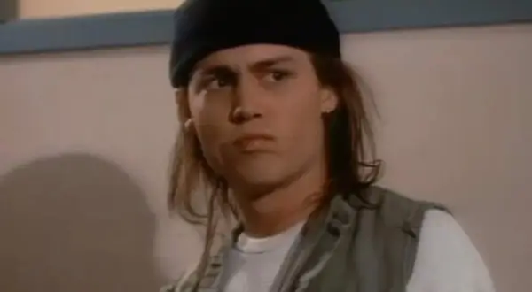 Johnny Depp ung med långt hår och svart mössa, bär en väst över en vit tröja.