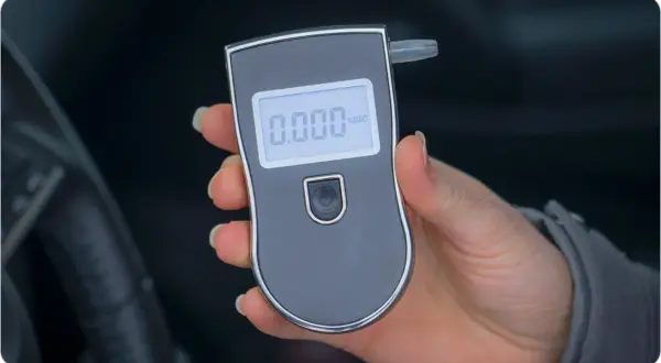 Dłoń trzyma alkomat z wyświetlaczem pokazującym 0.000.