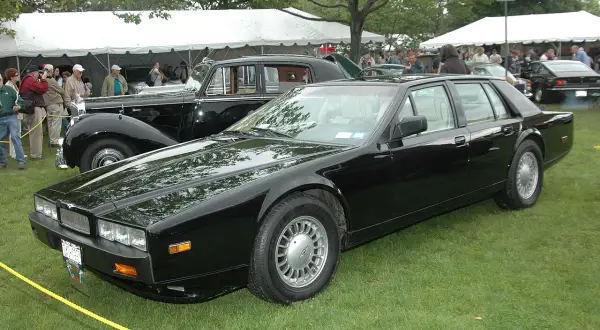 Svart Aston Martin Lagonda står på gräsmatta vid ett evenemang med tält och folk i bakgrunden.