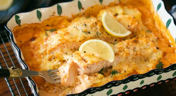 Ein köstlicher Lachs Auflauf mit geschmolzenem Käse und Zitronenscheiben, der gerade mit einer Gabel serviert wird.