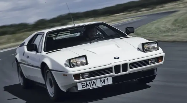 Białe BMW M1 z lat 80. pędzi po krętej drodze, ukazując swój kultowy design.