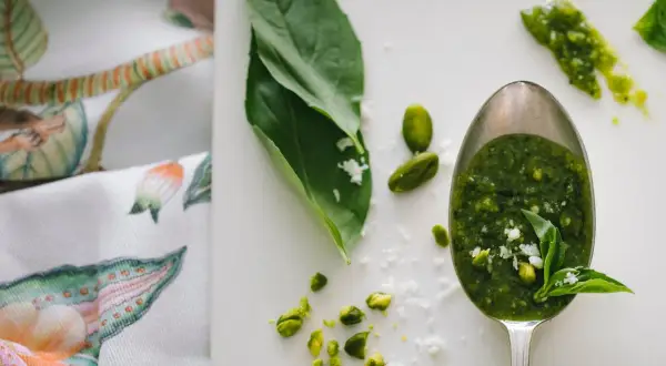Łyżka pełna aromatycznego pesto z rukoli, obok pistacje i listki bazylii.