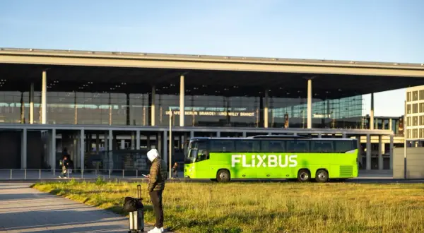 Mann mit Koffer wartet auf den Flixbus am Flughafen Berlin Brandenburg. Eine Direktverbindung Dresden Berlin Flughafen ist hier möglich.