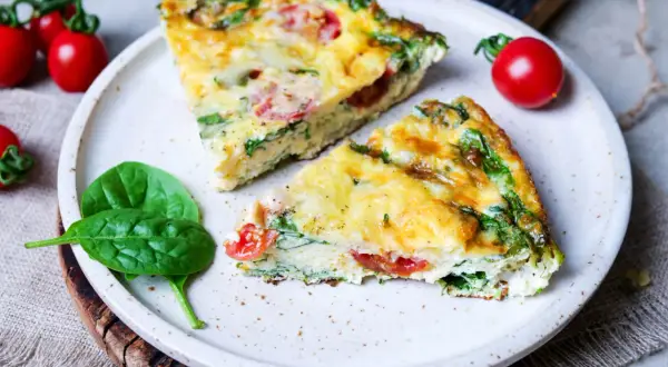 Zwei Stücke einer herzhaften Frittata mit Spinat und Tomaten auf einem Teller, garniert mit frischen Spinatblättern und Kirschtomaten. Ein köstliches Frittata Rezept.