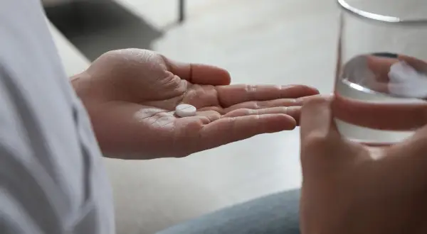 En hand håller en tablett, redo att sväljas med ett glas vatten. Detta kan vara en del av förklaringen till hur funkar antidepressiva.