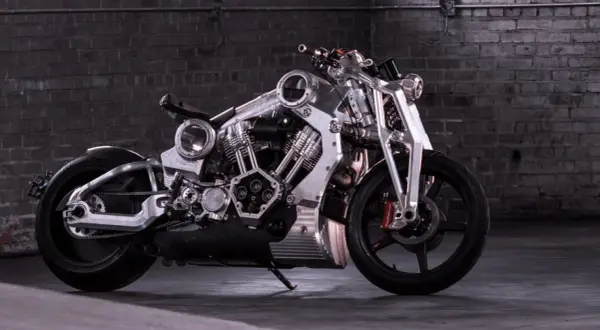 Wyjątkowy, lśniący motocykl, prawdopodobnie najdroższy motor na świecie, z masywnym silnikiem i detalami z polerowanego metalu, na tle ceglanej ściany.