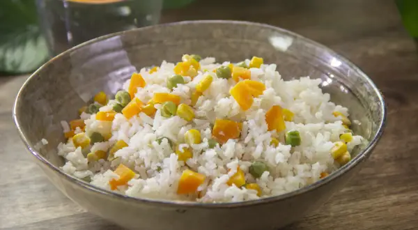 Un tazón de arroz blanco con trozos de zanahoria, guisantes y maíz. Un plato sencillo y delicioso de arroz con verduras salteadas.