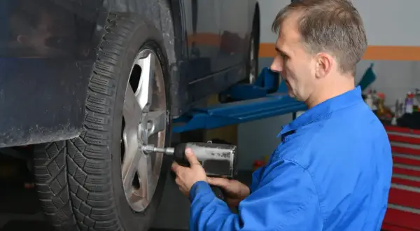 Mechanik w niebieskim kombinezonie dokręca śruby kół aluminiowych przy podniesionym samochodzie.