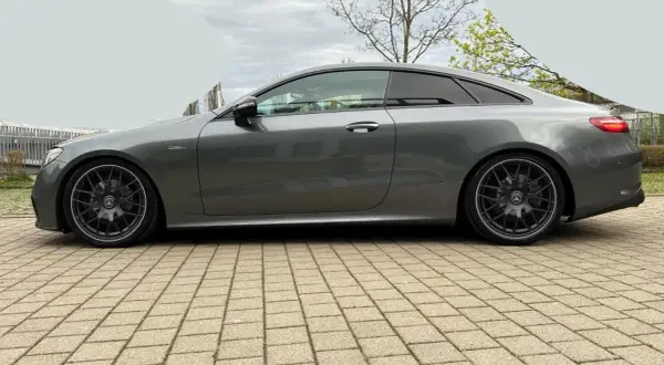Szary Mercedes-AMG E53 coupe z przyciemnianymi szybami i czarnymi felgami stoi na kostce brukowej.
