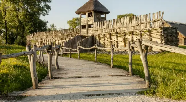 Drewniana kładka prowadzi do grodziska z wieżą obronną. To fragment szlaku piastowskiego, gdzie historia ożywa.