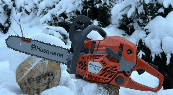 Pomarańczowa piła łańcuchowa Husqvarna 560 XP na tle zaśnieżonych drzew. Poznaj husqvarna 560 xp dane techniczne.