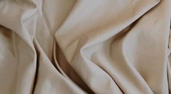 Sanfter, beige Stoff fällt in weichen Falten. Lyocell ist das, ein nachhaltiges Material, das sich so angenehm anfühlt.