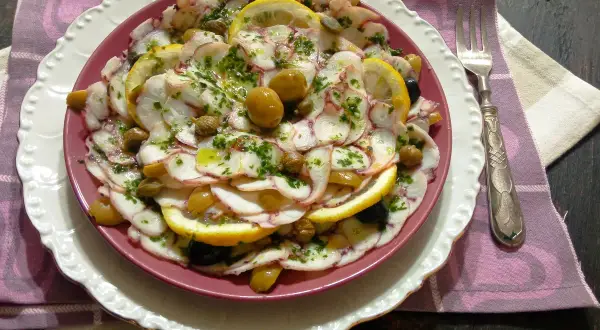 Delizioso carpaccio di polpo con limone, olive e capperi, condito con erbe fresche e olio d'oliva. Un piatto leggero e saporito.
