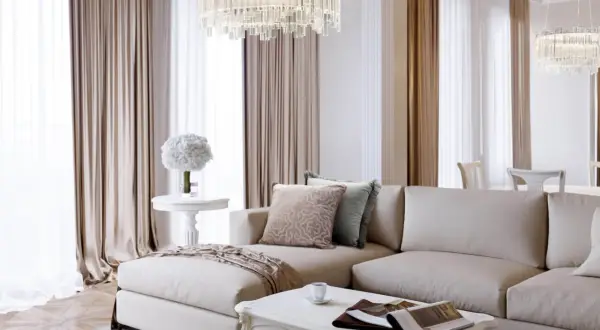 Elegancki salon w stylu modern classic z beżową sofą, kryształowym żyrandolem i jasnymi zasłonami.
