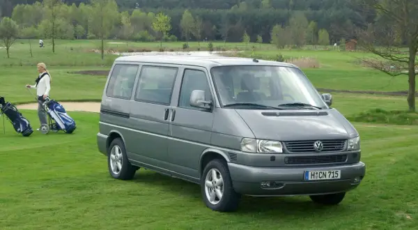 Szary VW T4 2.5 TDI 102KM na polu golfowym. Kobieta z kijami golfowymi obok.