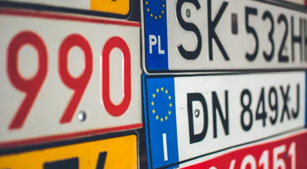 Zbliżenie na stos tablic rejestracyjnych z kodami krajów UE, w tym PL, SK i DN.