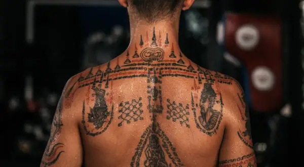 En rygg täckt av detaljerade sak yant muay thai-tatueringar, med symboler och skrifter som berättar en historia om styrka och skydd.