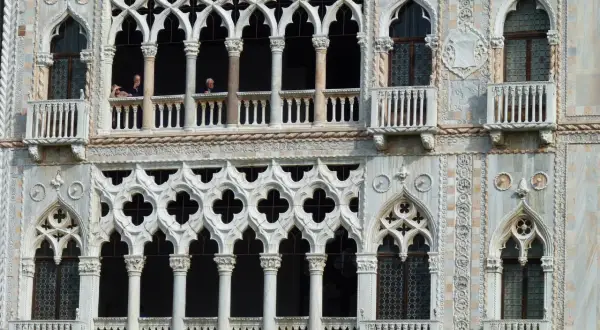 Dettaglio della Ca' d'Oro a Venezia, con le sue finestre traforate e balconi, dove si intravedono persone affacciate.