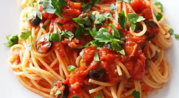 Pyszny makaron spaghetti z sosem pomidorowym, oliwkami i natką pietruszki. Czy makaron do spaghetti się płucze? Zazwyczaj nie, aby sos lepiej przylegał.