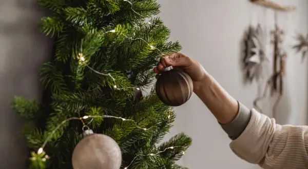 Eine Hand schmückt einen Wand-Weihnachtsbaum mit Kugeln und Lichterkette. So kann man einen Weihnachtsbaum selber machen, auch ohne Platz.