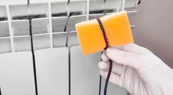 Guanto bianco e spugna arancione legata con cordino colorato, pronti per pulire i termosifoni.