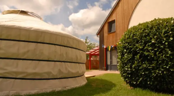 Une yourte alsace, à côté d'une maison en bois, sous un ciel bleu et nuageux.